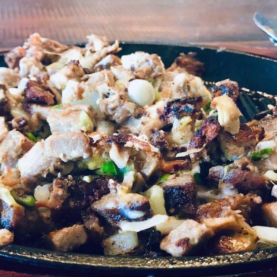 Grilled mixed meat and vegetables topped with creamy sauce and herbs on a black serving platter.